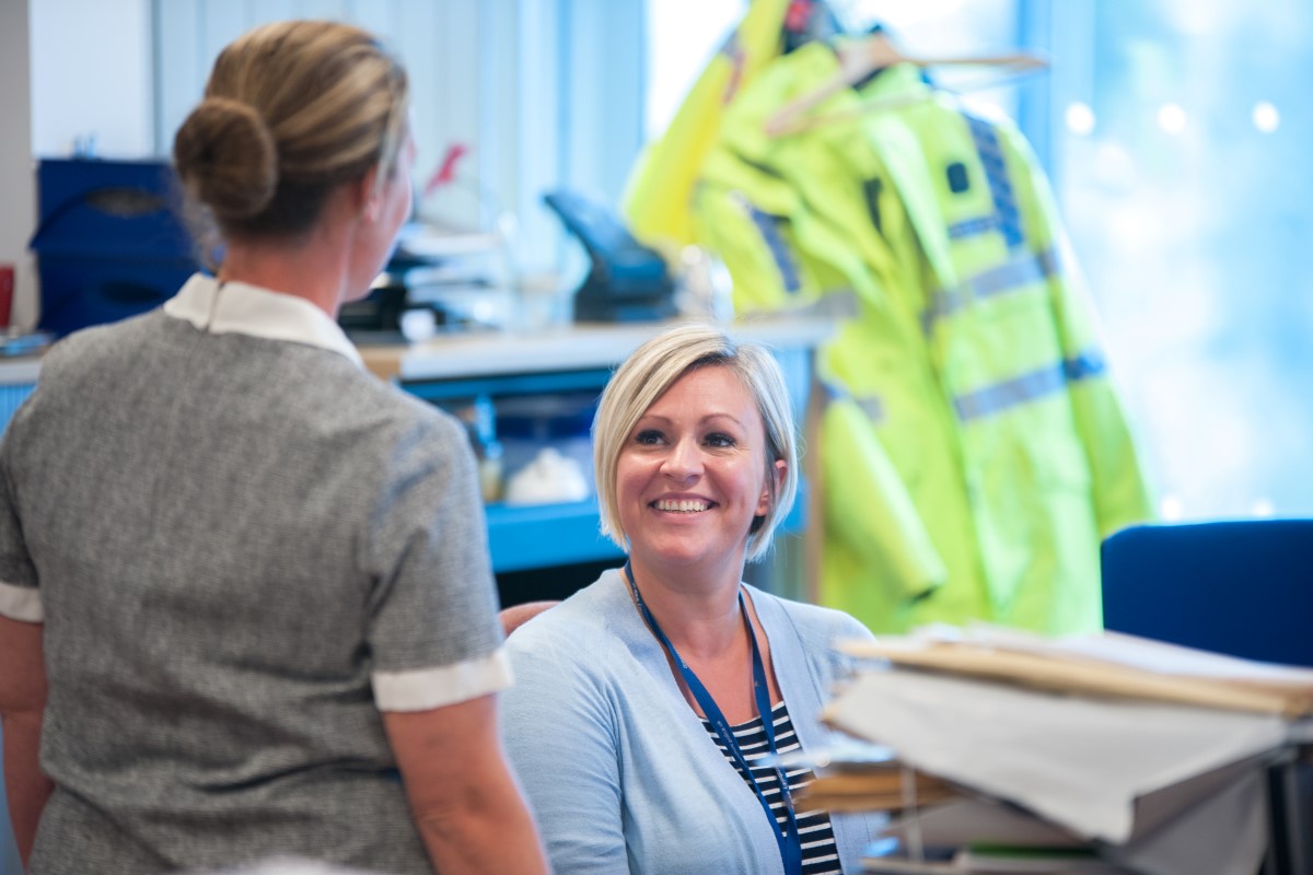 Femal police staff member sat at her desk smiling at a colleague.