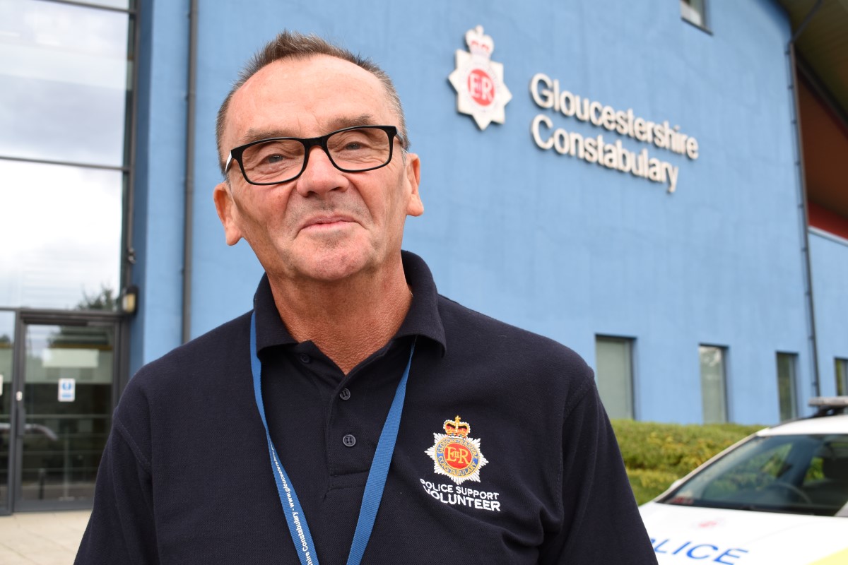 Male police volunteer smiling with Gloucestershire Constabulary HQ in the background.